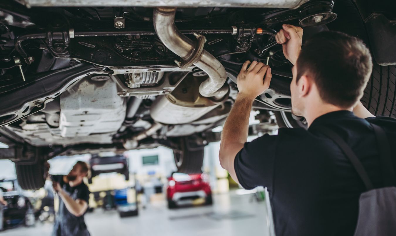 Ein Mechaniker schraubt am Unterboden eines Autos
